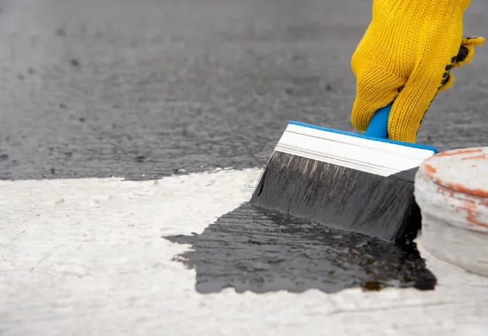 Personne qui applique une résine d'étanchéité noire sur une surface à l'aide d'un pinceau