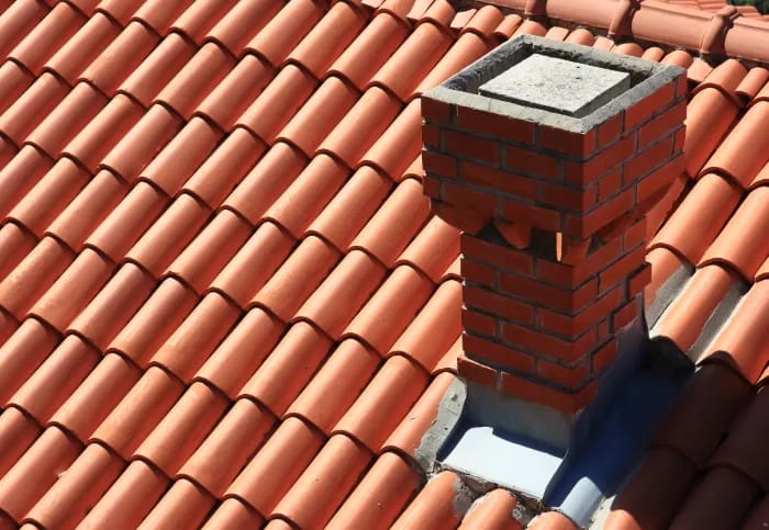 Toit en tuiles d'argile orange avec une cheminée en briques, des fenêtres et un ciel bleu avec des nuages blancs